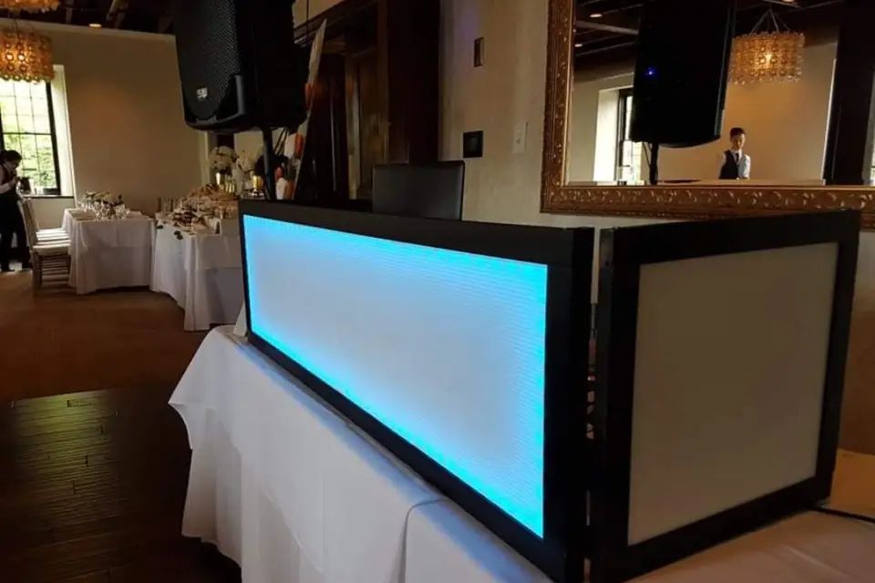 The DJ booth lit teal at the edge of a reception hall dance floor